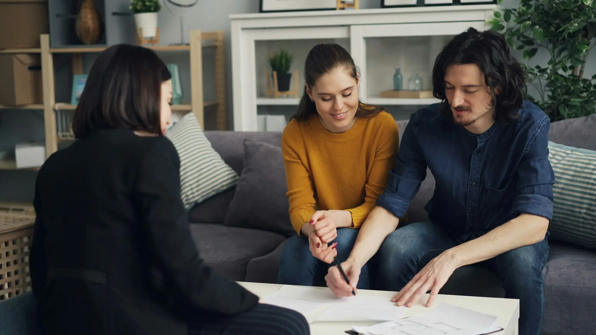 Couple signing documents with an adviser at the dining table
