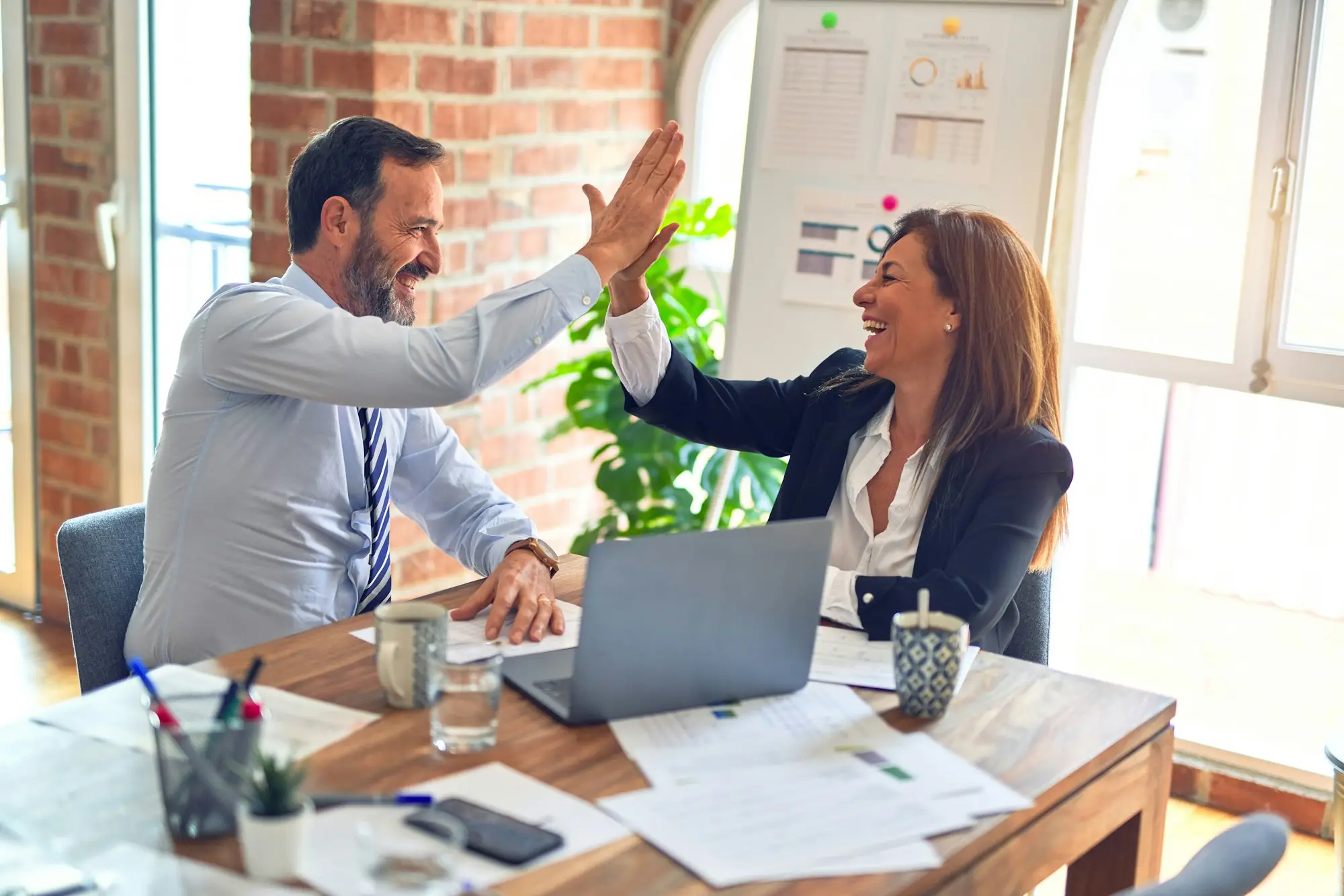 Two business owners high-fiving at a meeting table